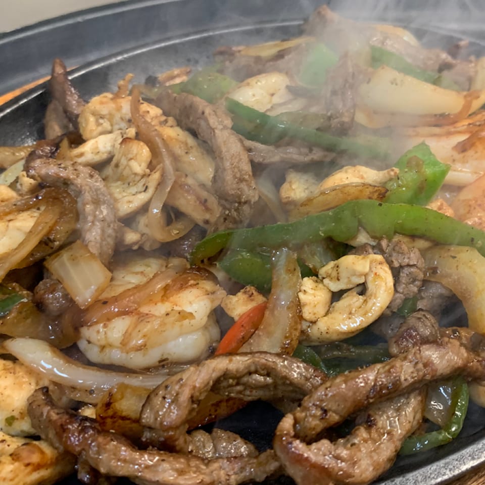 Sizzling fajitas with steak, chicken, shrimp, onions, and green peppers on a hot skillet.