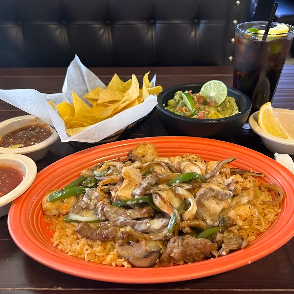 A vibrant Mexican meal with fajitas, rice, chips, salsa, guacamole, and a drink on a wooden table.