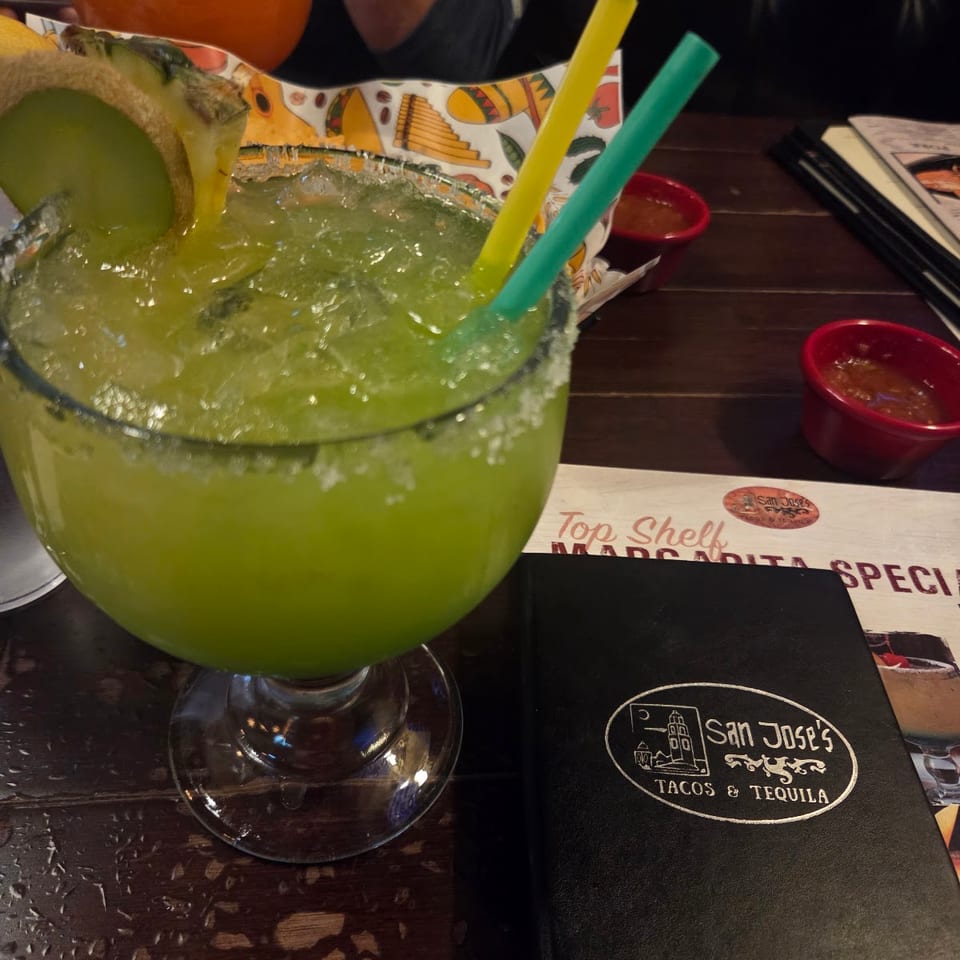 A large green margarita with fruit garnish and a San Jose's Tacos & Tequila menu.
