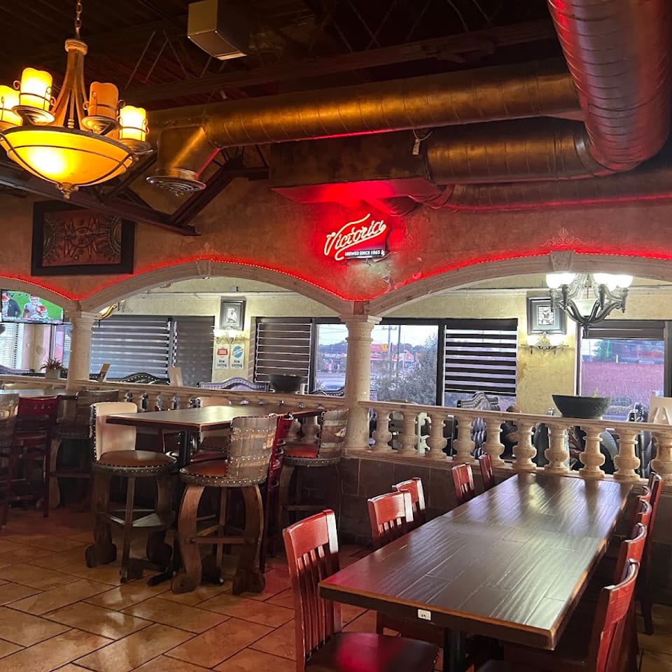 Restaurant interior with red neon lighting, arched doorways, and a mix of high-top and dining tables.