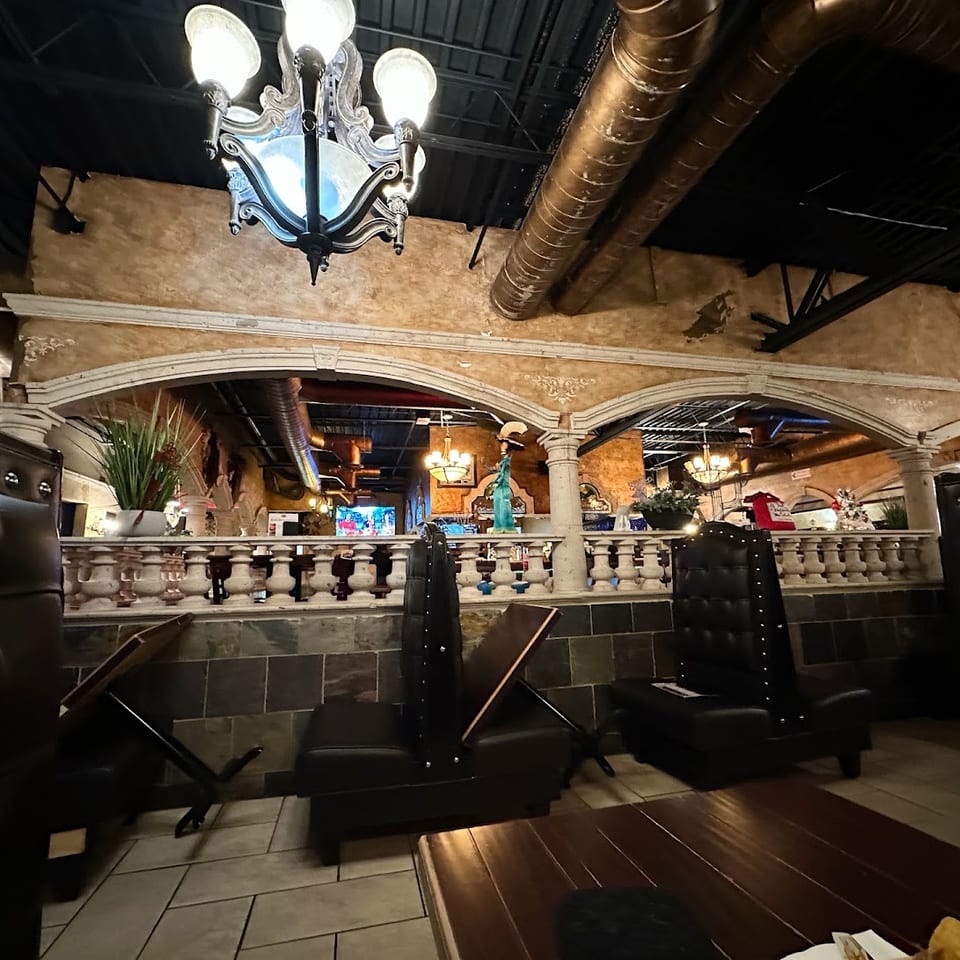 Restaurant interior with dark leather booths, ornate chandelier, and arched balcony overlooking dining area.